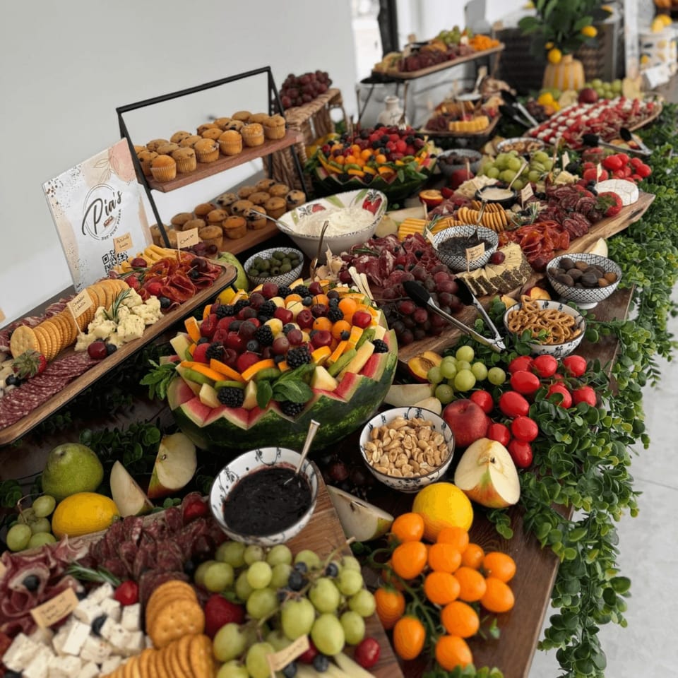 A long table laden with a vibrant Italian buffet of fruits, cheeses, meats, and pastries.