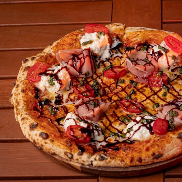 Pia's Not Just Pizza's Italian pizza with prosciutto, burrata, cherry tomatoes, pesto, and balsamic glaze.