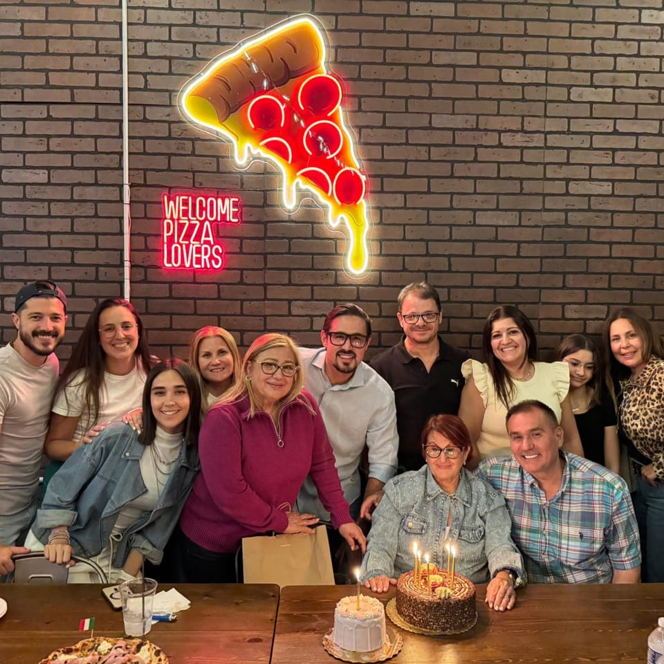 A large group of people celebrating a birthday with cakes at Pia's Not Just Pizza.