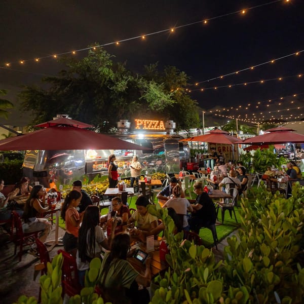 Pia's Not Just Pizza outdoor dining area at night, with a pizza food truck and string lights.