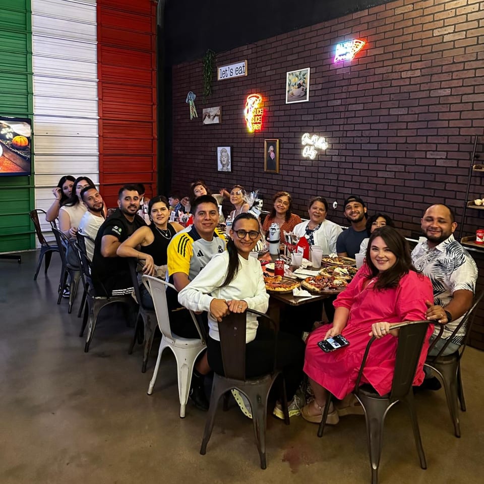 A large group of people smiling and sitting around tables with pizzas at Pia's Not Just Pizza.