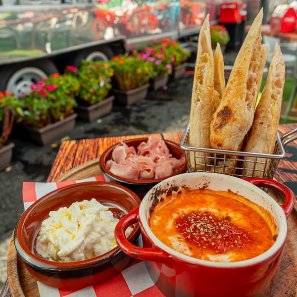 Baked cheese and tomato dip, prosciutto, ricotta, and breadsticks on a wooden board.