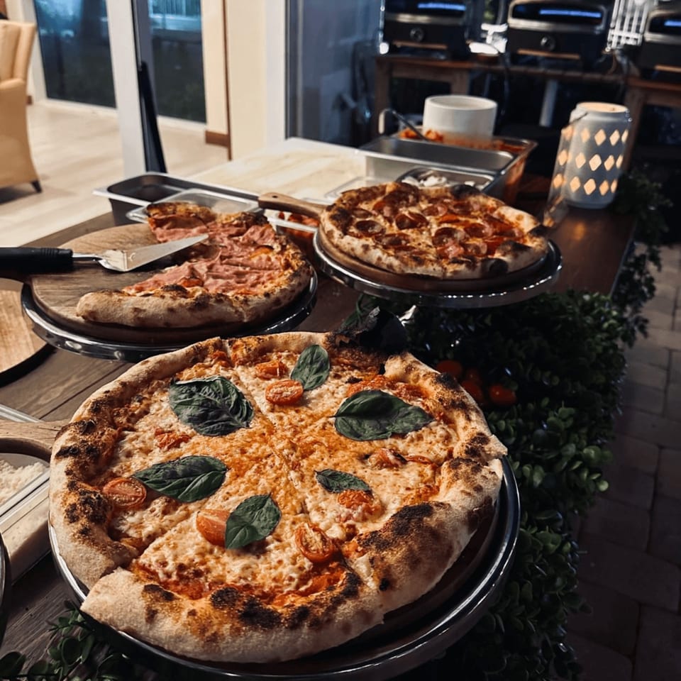 Three Pia's Not Just Pizza pizzas, including Margherita and pepperoni, on a buffet table with greenery.