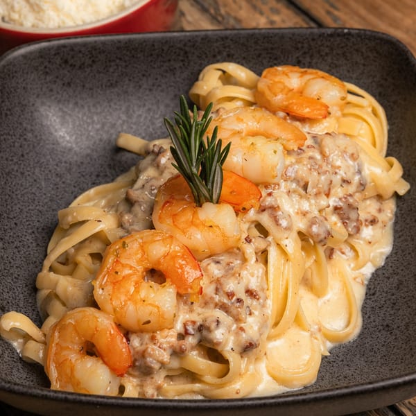 Creamy Italian tagliatelle pasta with shrimp and rosemary in a dark bowl, with grated cheese in the background.